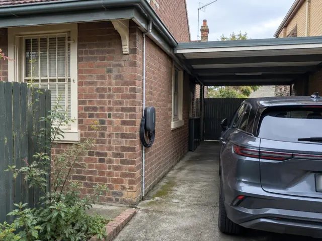 Wall-mounted EV charger on a brick house wall beside a driveway and carport in Rozelle